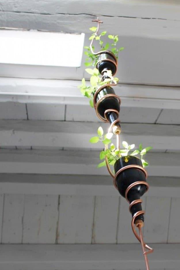 DIY herb garden from wine bottles, black painted bottles hung in a vertical line on copper tubing with green sprouts