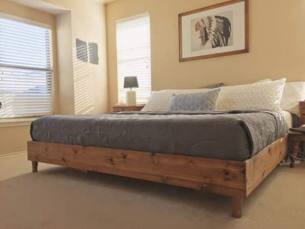 DIY king bed frame in stained wood with a low platform base and grey bedding in a neutral beige bedroom