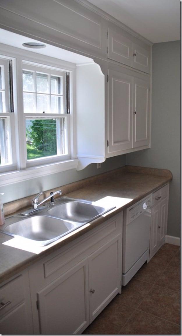 Galley kitchen with white cabinets carrying added molding panels, a laminate counter, double stainless sink and grey walls