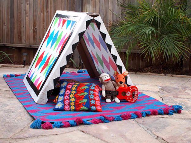 Cardboard craft A frame play tent painted with chevrons and diamonds on a patio rug with soft toys inside