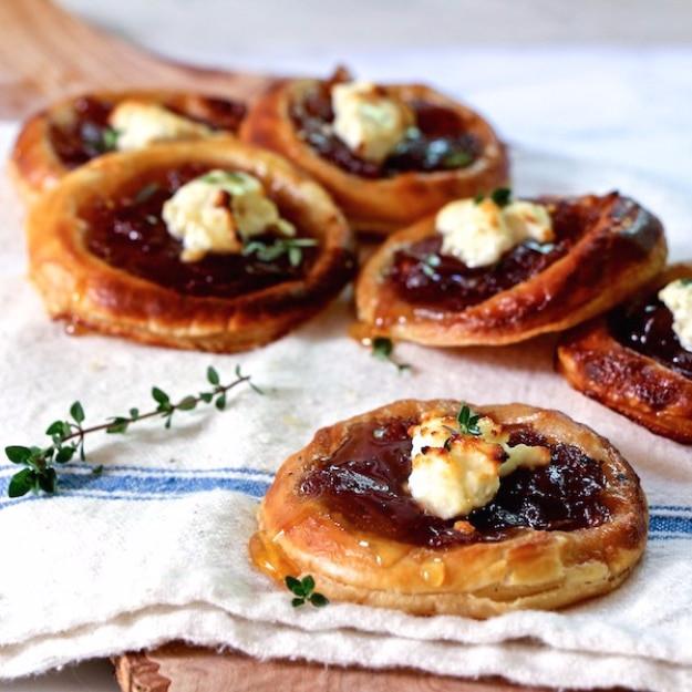 Caramelized onion and feta tartlets party appetizer on puff pastry with thyme leaves and a honey drizzle