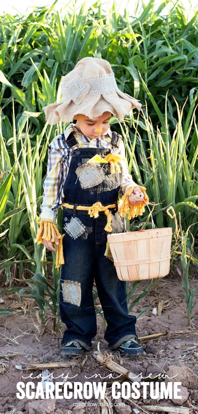 Child wearing patched denim overalls, plaid shirt, burlap scarecrow hat and yarn cuffs while holding a wood basket