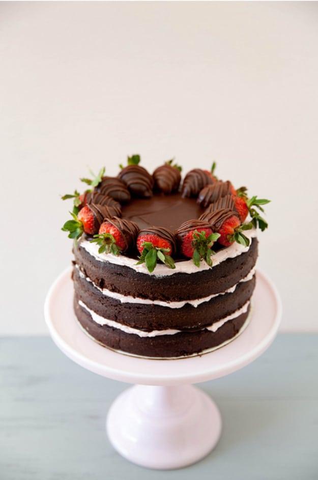 Naked chocolate layer cake with white cream between the layers and chocolate dipped strawberries on top