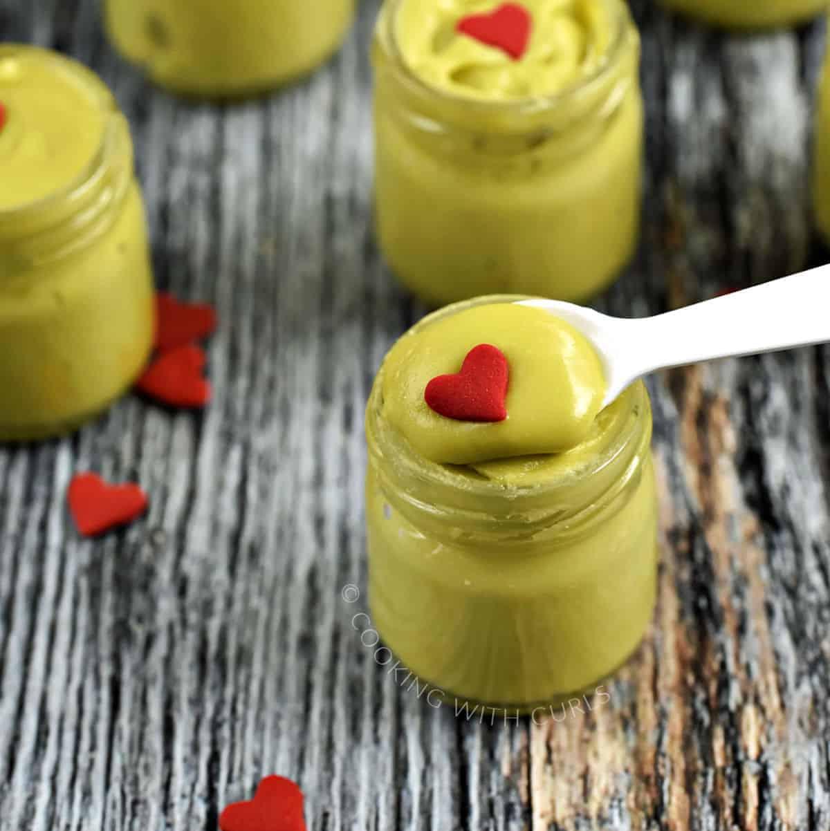 Tiny glass jars of bright green spoon fudge topped with sprinkles, with spoons resting beside them on a board