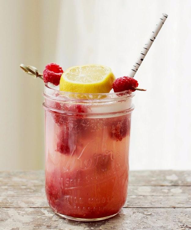 Raspberry lemonade cocktail in a glass jar topped with a lemon wheel, fresh raspberries and a paper straw