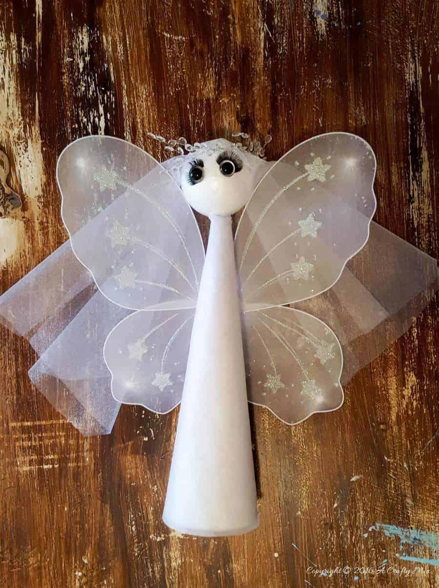 White Christmas angel with a gauze wrapped cone body, sheer fairy wings and a round head with big eyes on dark wood