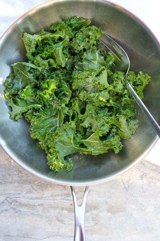 Braised kale wilted bright green in a pale grey green skillet with a long handle and a spoon resting on marble