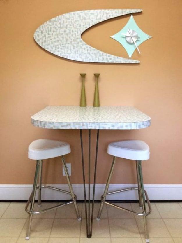 Mint and cream boomerang clock on a peach wall above a small laminate snack bar on hairpin legs with two vinyl stools