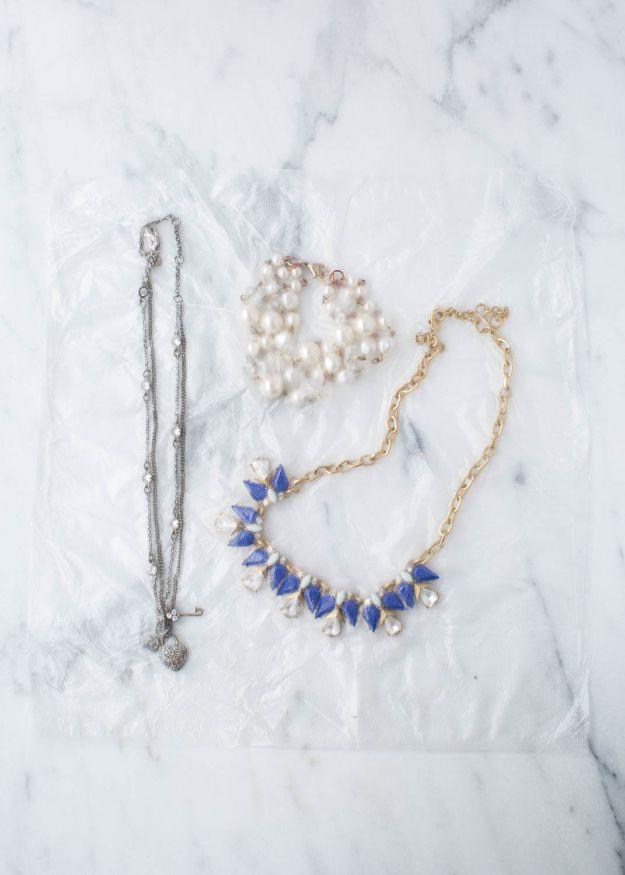 A silver chain, a pearl necklace and a blue stone statement necklace laid on a sheet of cling wrap on marble