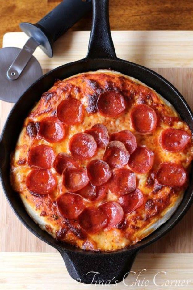 Cast iron skillet pizza topped with sauce and a full layer of pepperoni beside a pizza wheel on wood