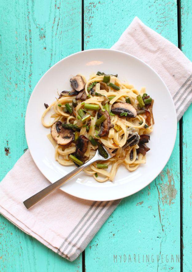 Vegan fettuccine alfredo with sliced mushrooms and asparagus on a white plate over a mint green wood table