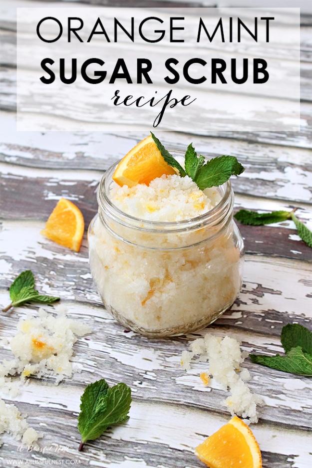 Orange mint sugar scrub in a small mason jar with fresh orange wedges and mint leaves on weathered white wood