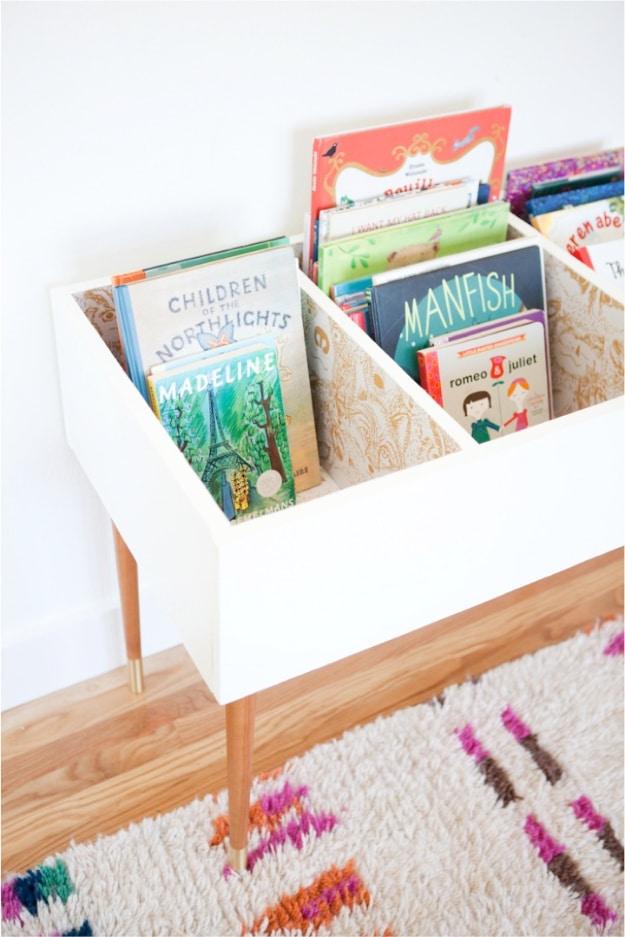 DIY kids book bin, a white three bay box on tapered wood legs holding picture books face out on a patterned rug