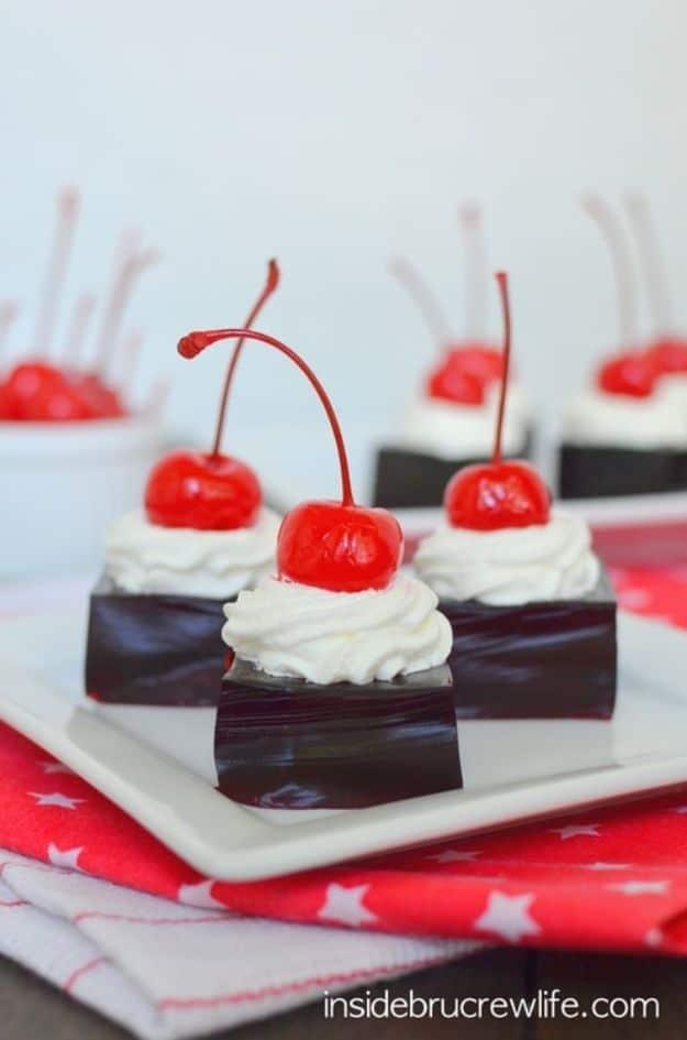 Cherry Dr Pepper jello squares cut into cubes on a plate, each topped with whipped cream and a cherry