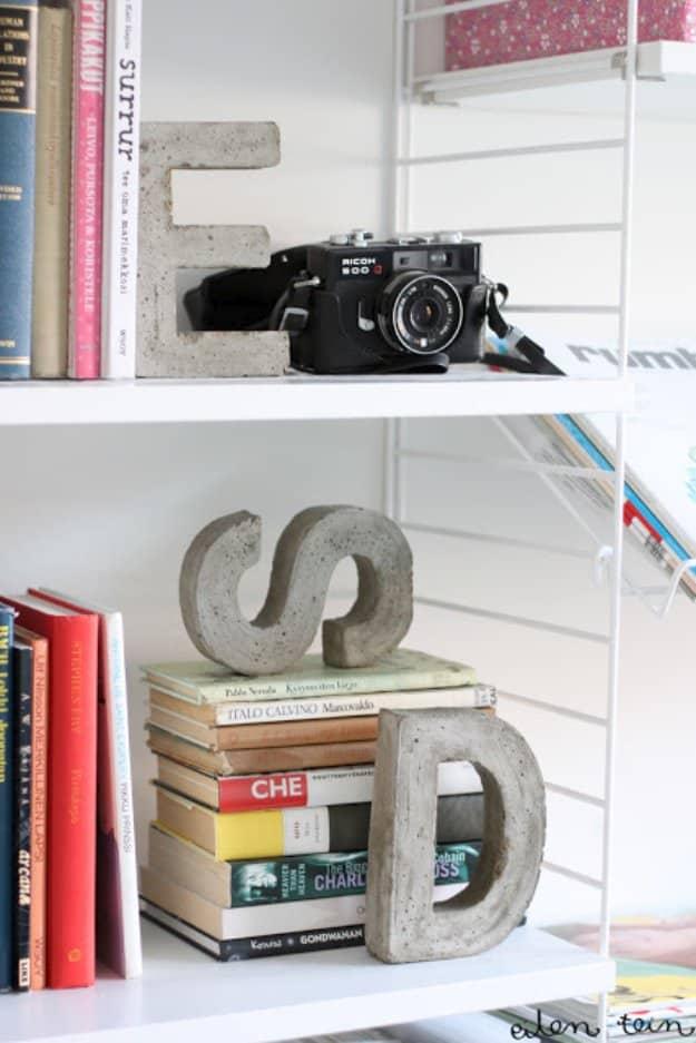 Concrete monogram bookends, cast cement letters E, S and D standing on white shelves beside books and a camera