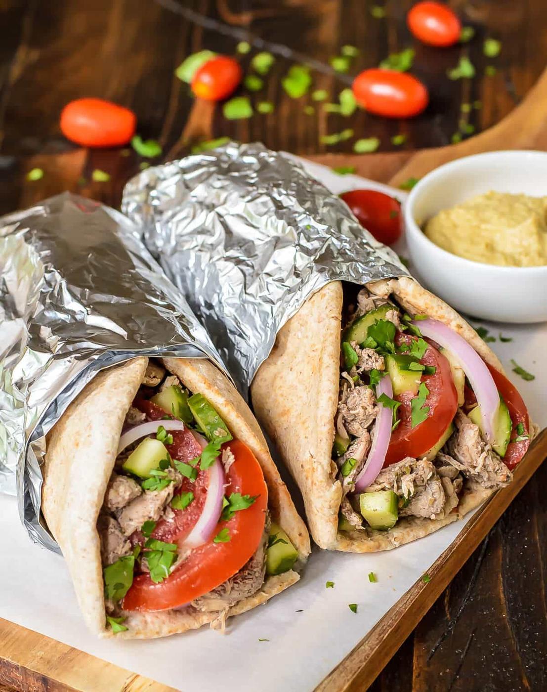 Chicken shawarma wraps in foil cut open to show spiced chicken, tomato, cucumber and red onion on a board