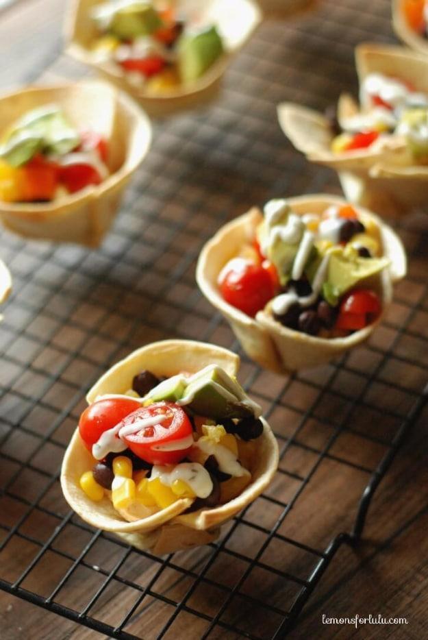 Mini taco tortilla cups on a wire rack, crisp shells filled with black beans, corn, tomato and avocado