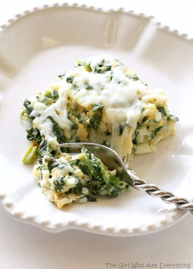 A forkful of cheesy spinach parmesan rice bake lifted from a serving on a white scalloped edge plate