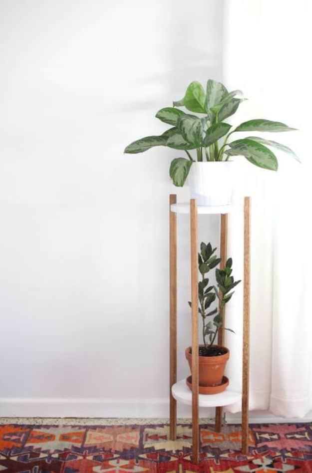 Tall two tier plant stand with slim wood uprights and round white shelves holding a leafy plant and a terracotta pot