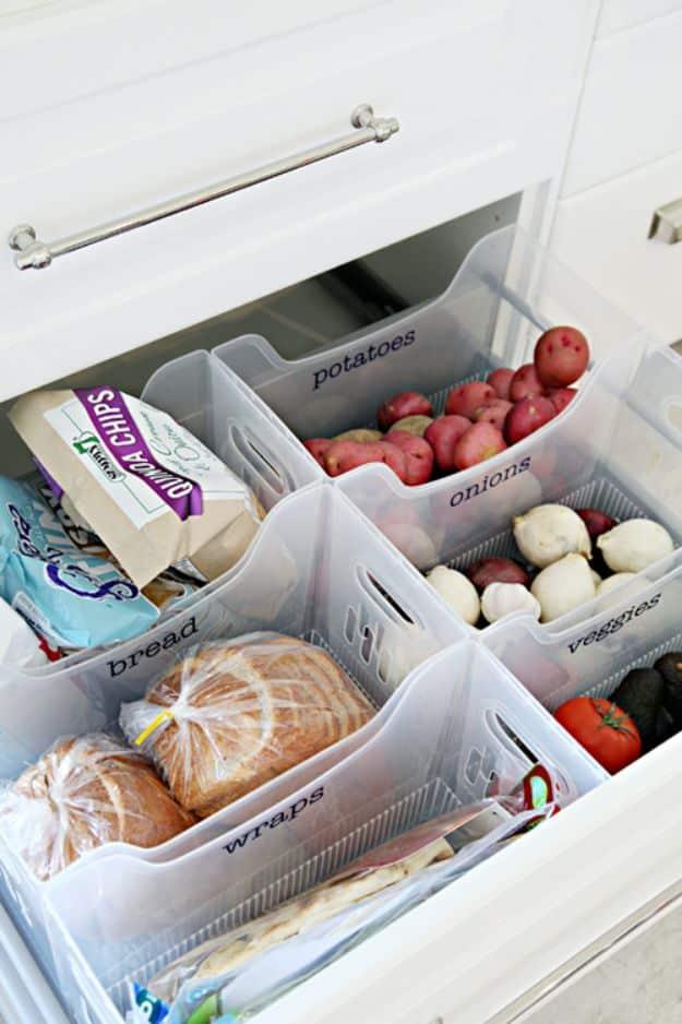 Open pantry drawer fitted with clear handled bins labeled potatoes, onions, bread, wraps and veggies, full of food