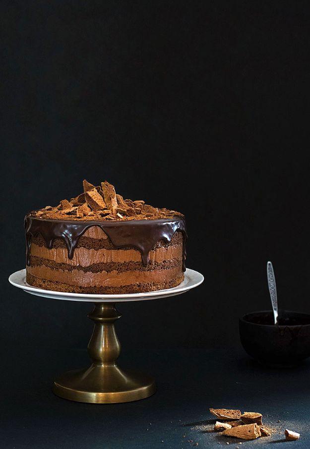 Pure chocolate mousse cake on a brass stand against a dark background with chocolate shavings piled on top