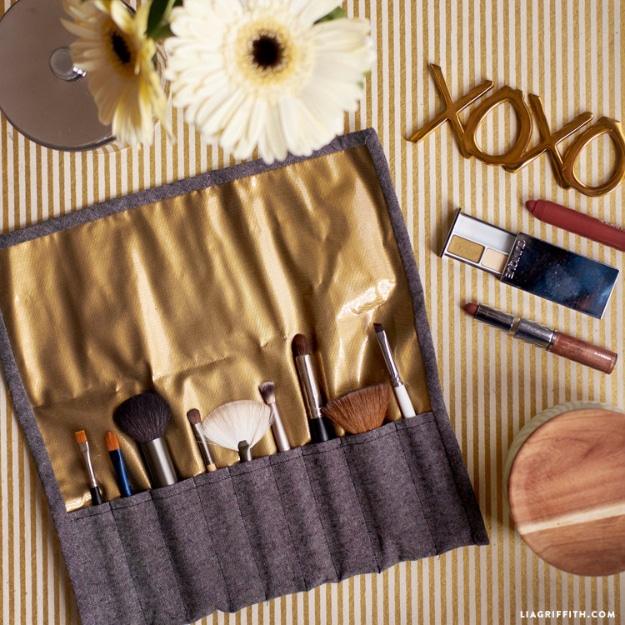 Makeup brush roll in gray linen with gold oilcloth lining, open flat with seven brushes in individual pockets