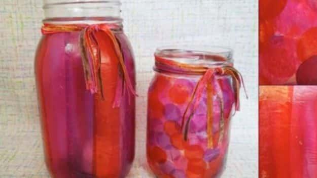 Two mason jars decoupaged with overlapping pink, red and purple tissue paper squares, with fabric ties at the necks
