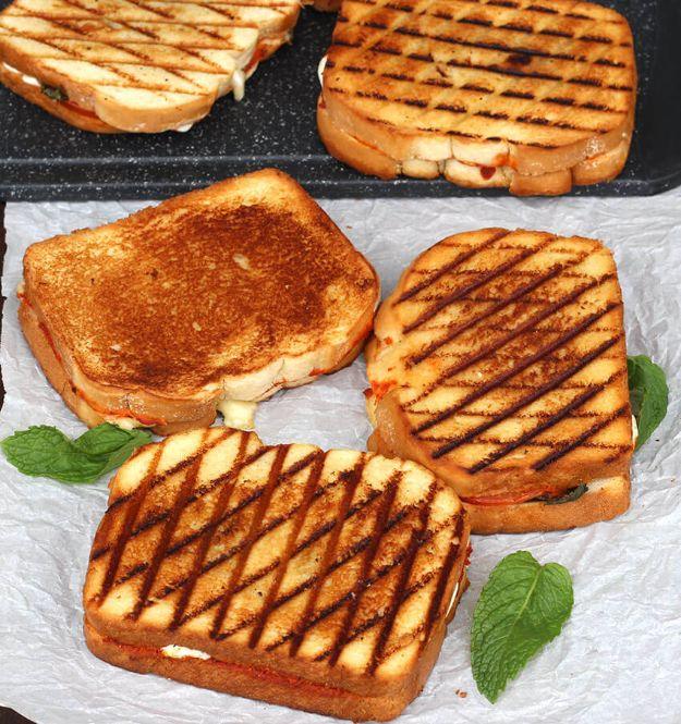 Grilled margherita sandwiches on a griddle with dark grill marks, basil leaves scattered around them