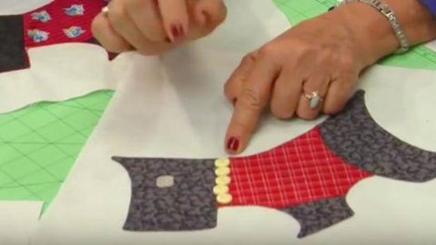 Video still of a quilt top with appliqued grey and red plaid Scottie dogs, two hands positioning a piece of fabric