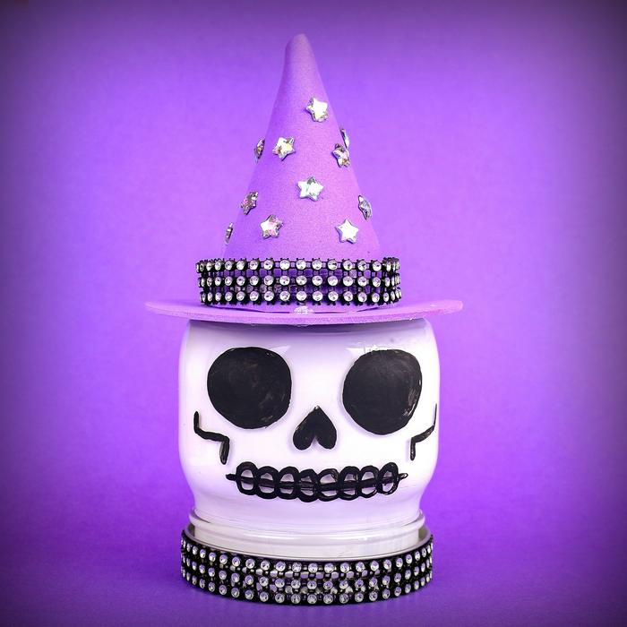 White painted skull mason jar wears a purple craft foam witch hat with black details and sparkling rhinestones