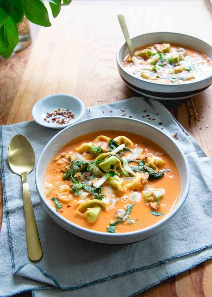 Creamy tomato tortellini soup with cheese tortellini, baby spinach and grated cheddar in a white bowl
