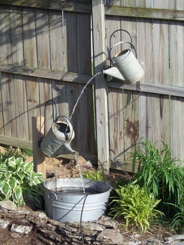 Two galvanized watering cans mounted on a weathered fence pouring water down into a galvanized tub below