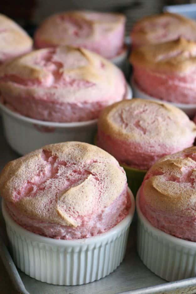 Strawberry pudding souffles risen high above fluted ramekins on a baking sheet, pale pink with browned tops