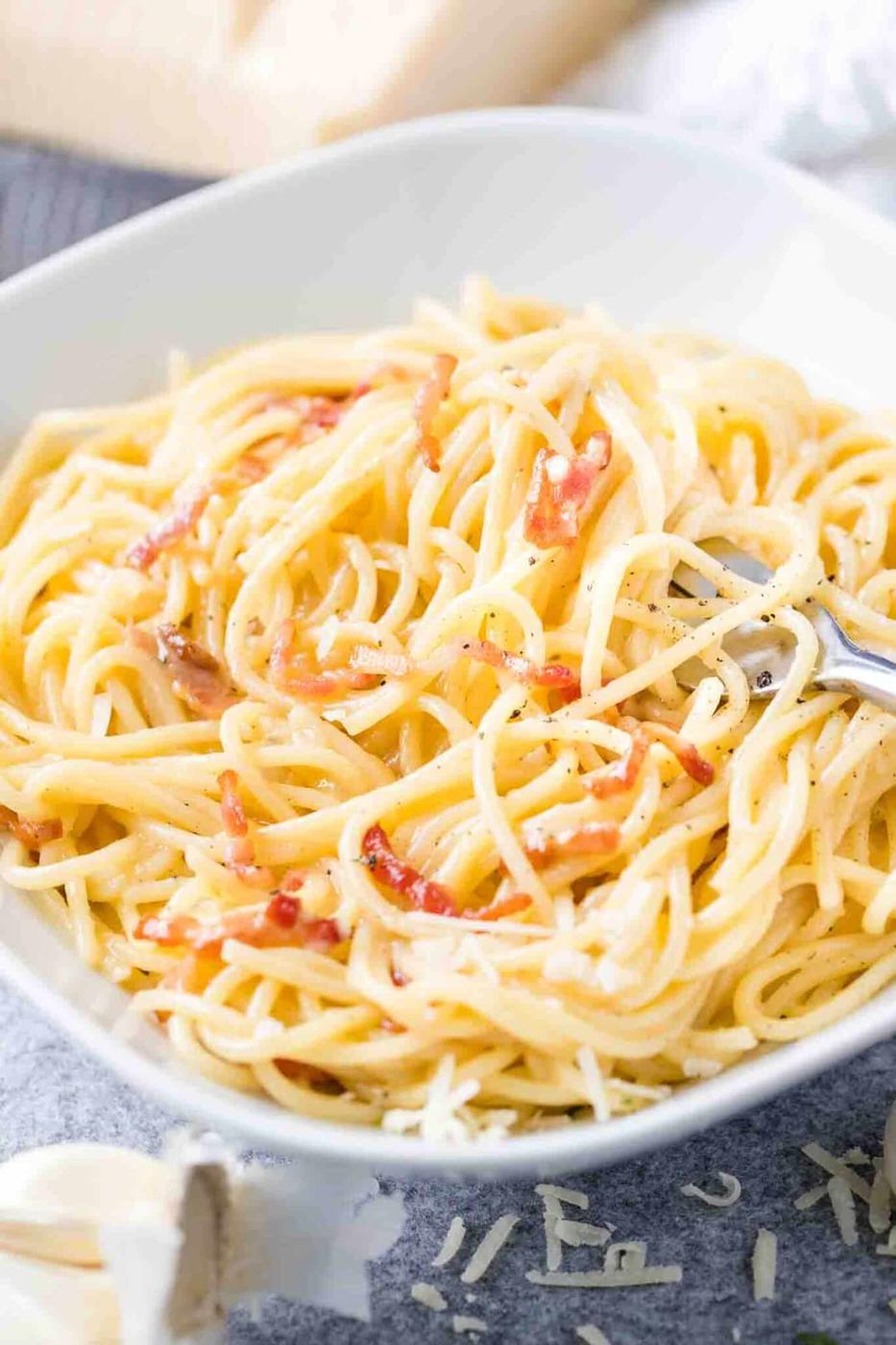 Pasta carbonara in a skillet with crisp bacon, a glossy egg and parmesan sauce and cracked black pepper