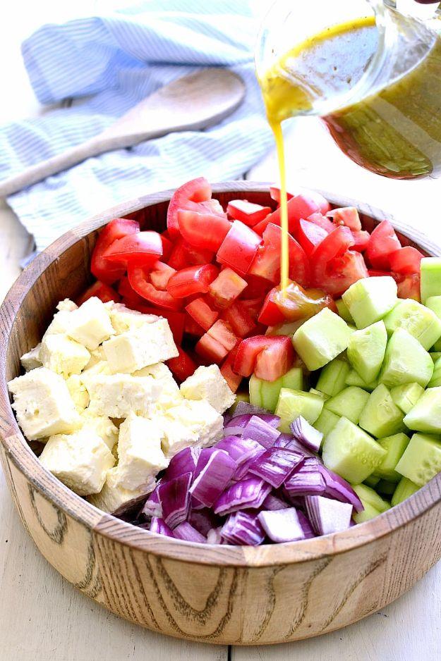 Tomato cucumber and feta salad with red onion in a wooden bowl as the dressing is poured over the top