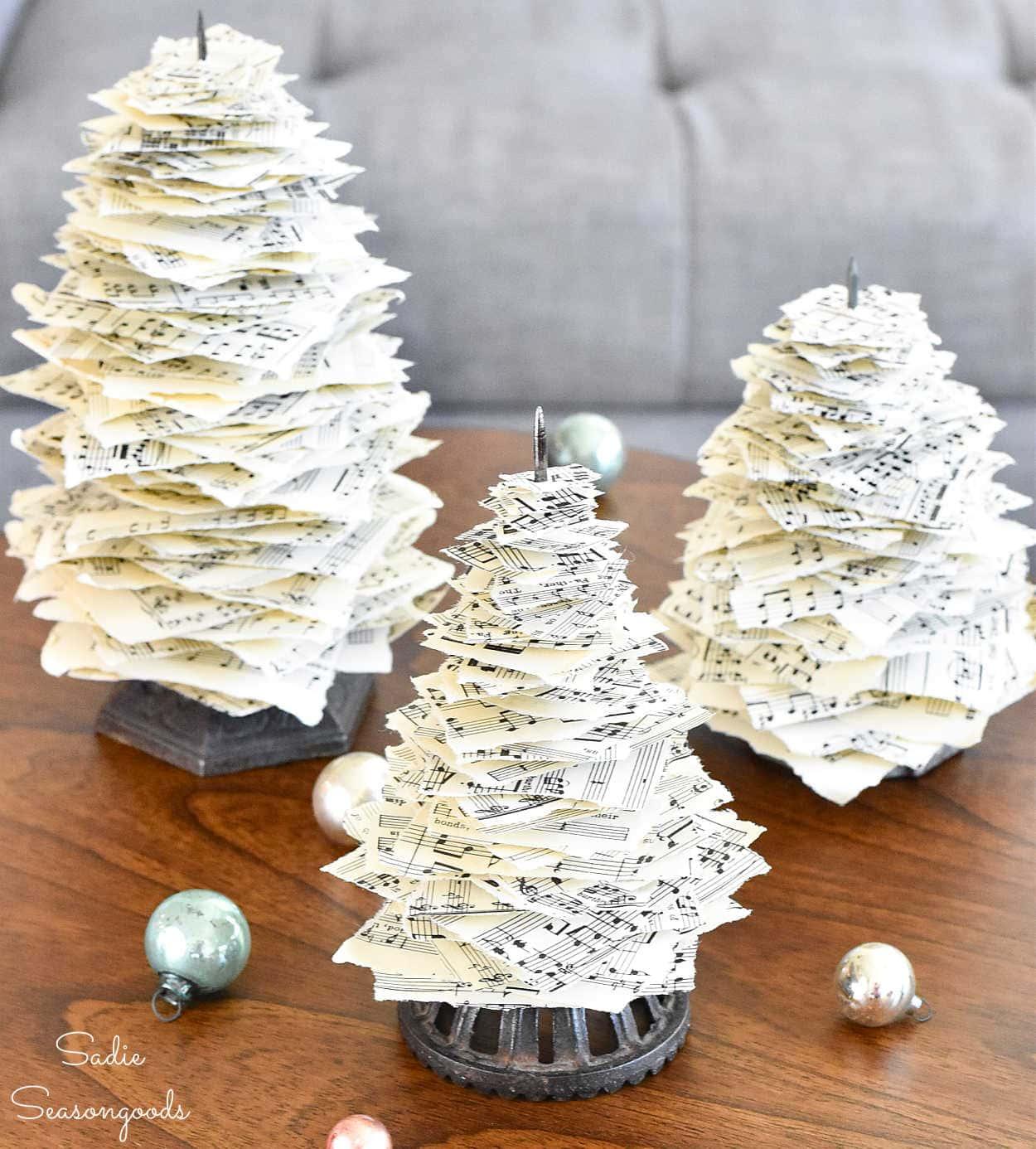Three Christmas trees made from torn sheet music squares stacked on vintage receipt spikes beside silver ornaments