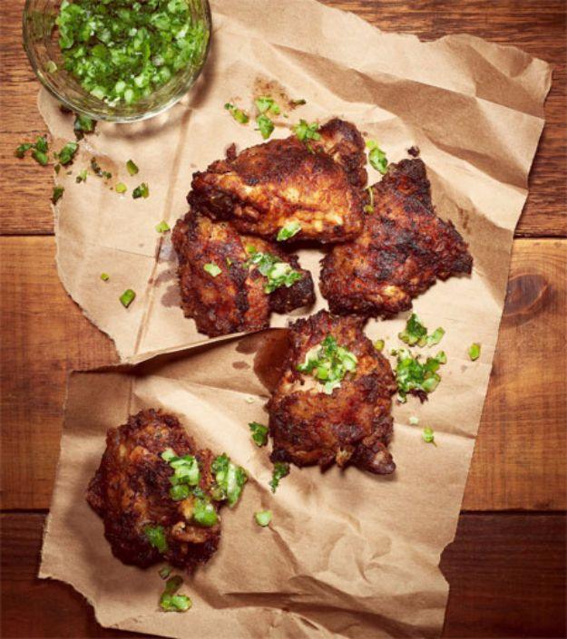 Coca Cola brine fried chicken, craggy dark fried thighs resting on brown parchment paper scattered with chopped chives