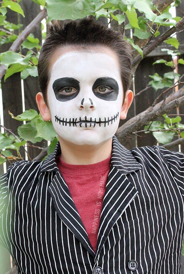 Jack Skellington Halloween makeup on a boy with white face paint, black sunken eyes and a stitched grin