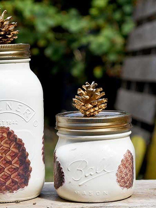 Cream painted mason jars decoupaged with vintage pine cone images, one topped with a small gold pine cone