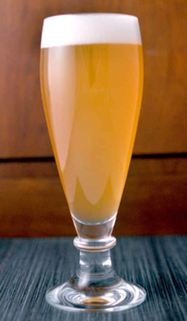 Passionfruit and mango wheat beer in a glass, hazy pale orange, with fresh mango slices beside it and passionfruit