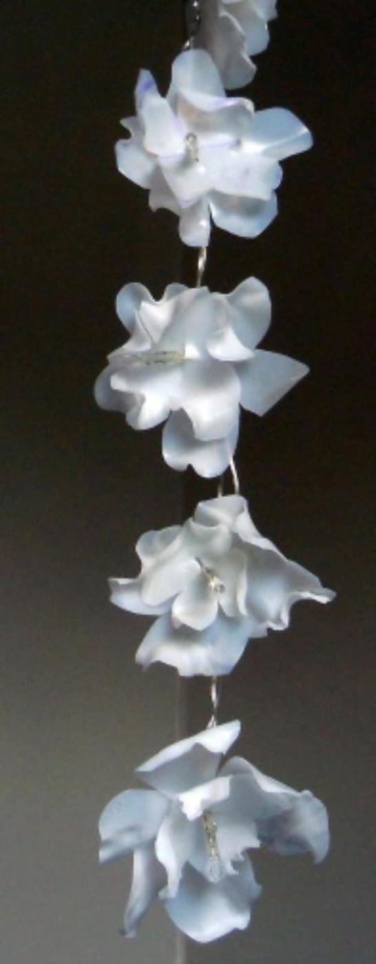 String of white flowers cut and heat shaped from a milk jug, lit from within by LED fairy lights against a dark background