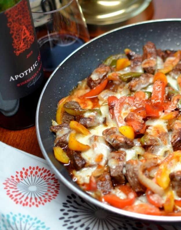 Philly steak and cheese skillet of beef and peppers under melted provolone, a red wine bottle beside it