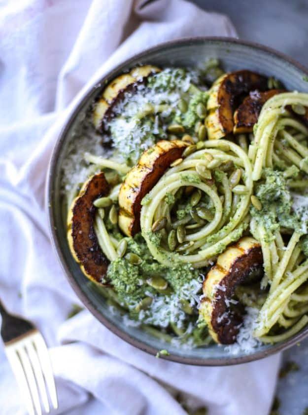 Pumpkin seed pesto pasta in a dark bowl with caramelized delicata squash rings and plenty of grated parmesan