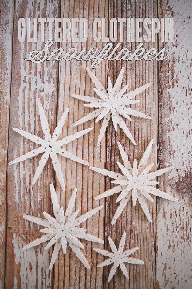 Five white glittered clothespin snowflakes in two different sizes laid out on chippy painted wood boards