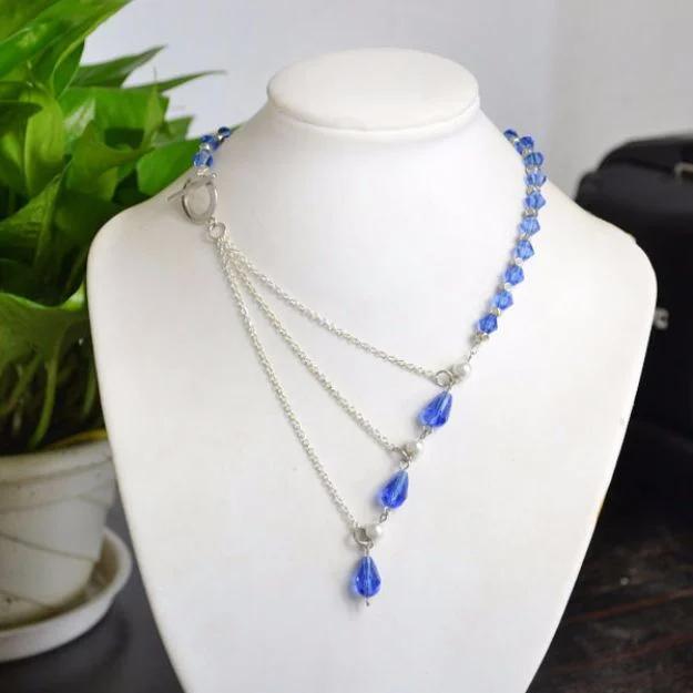 Ocean style chain link necklace, three silver chains on a white bust with blue crystal beads and a hanging teardrop
