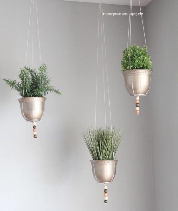 Three metallic spray painted hanging planters on twine with wooden beads holding greenery on a white wall