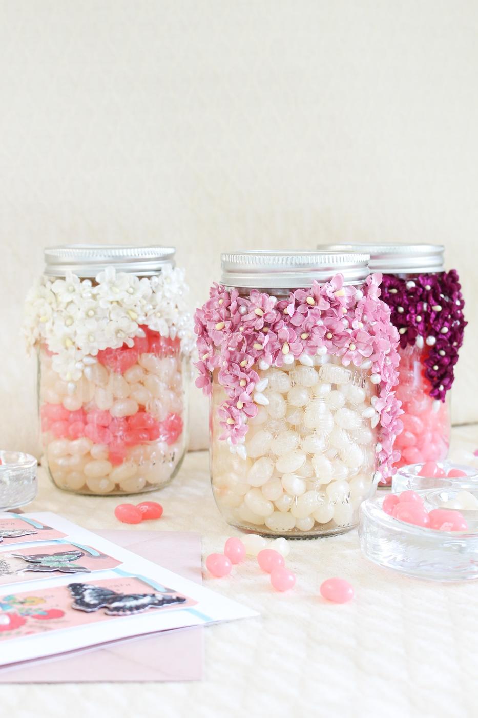 Canning jar decorated with a cascade of small faux flowers and pearls, filled with pink candy and a paper lid