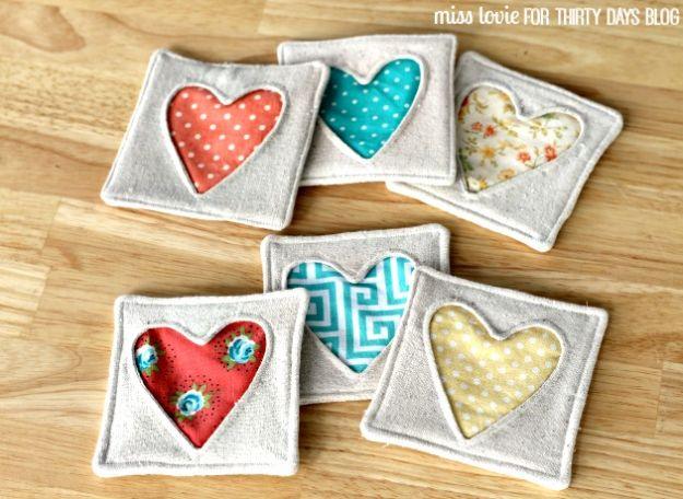 Padded heart coasters quilted from mixed cotton fabric scraps, a set of four stacked beside a mug on a wooden table