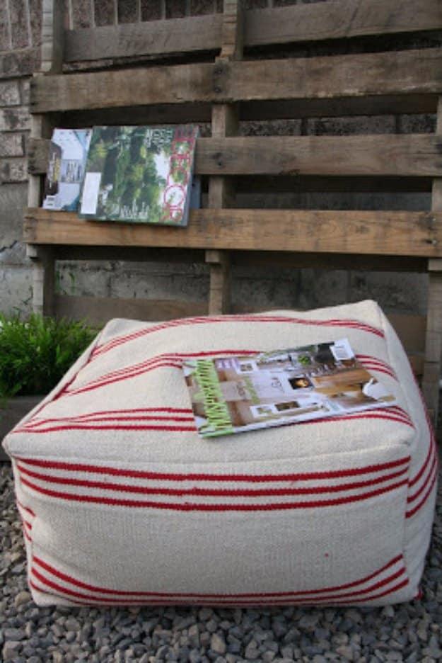 Cream and red striped floor pouf made from IKEA floor mats, sitting outdoors on gravel against a wooden pallet wall