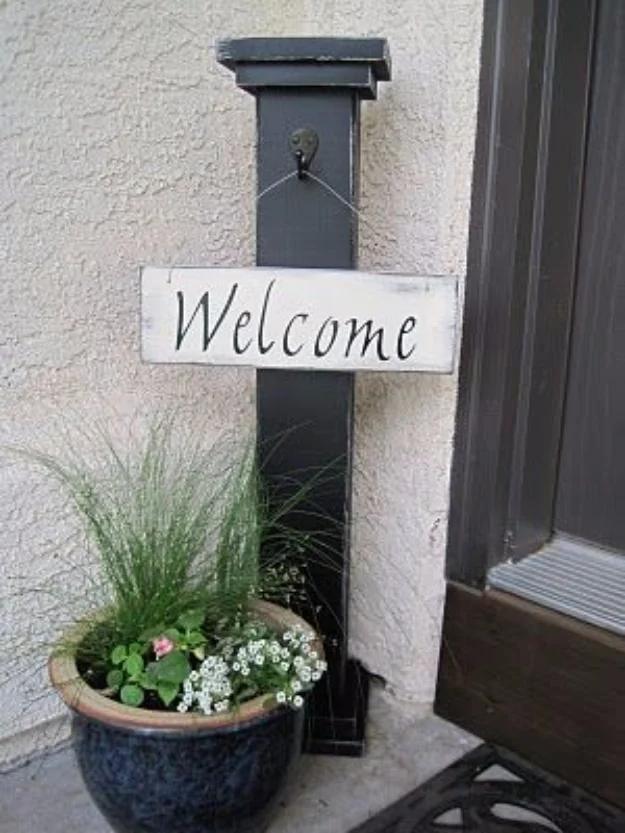 DIY curb appeal welcome column in distressed black with a hanging white welcome sign set in a blue planter by a door